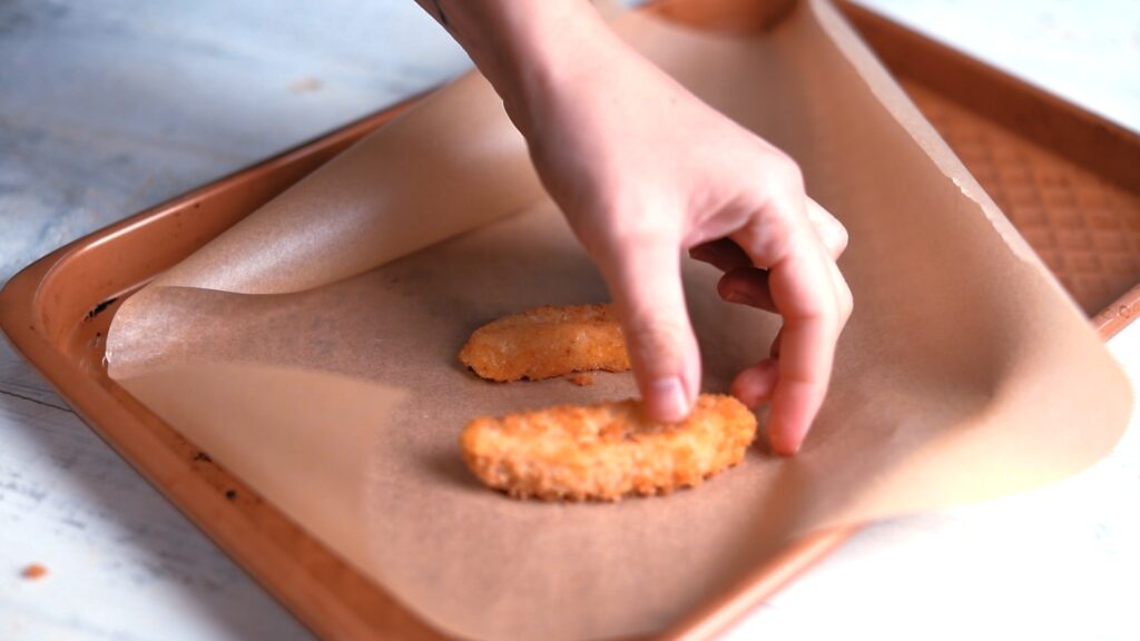 Overhead shot of hands placing chicken nuggets on a wooden kitchen counter.