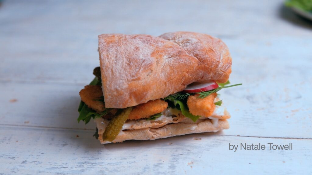 The completed gourmet sandwich, beautifully arranged on a wooden table, showcasing its delectable ingredients and expertly crafted presentation via professional video editing.